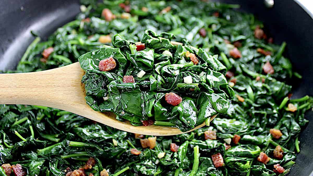 Sauteed Spinach with Pancetta held up out of skillet with wooden spoon