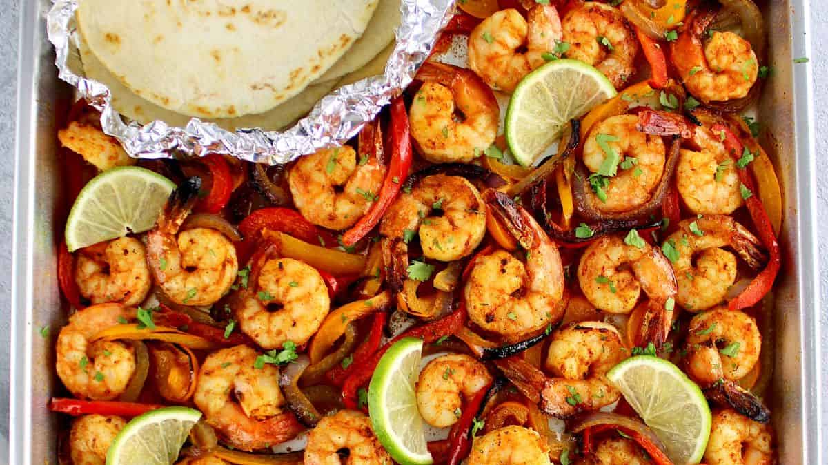 Sheet Pan Shrimp Fajitas with tortillas in foil and slices of lime