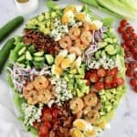 overhead view of Shrimp Cobb Salad in oval platter with dressing annd veggies in background