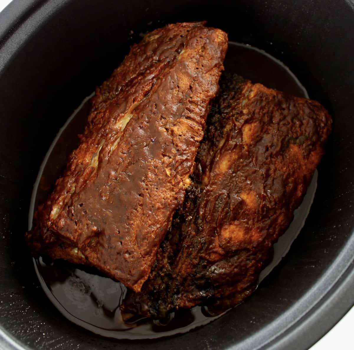 2 half baby back ribs racks in slow cooker with bbq sauce cooked