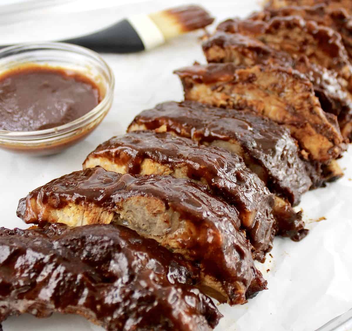 Slow Cooker Baby Back Ribs cut up on baking sheet with brush and bbq sauce in back