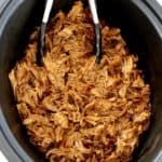 pulled pork in slow cooker insert with black tongs