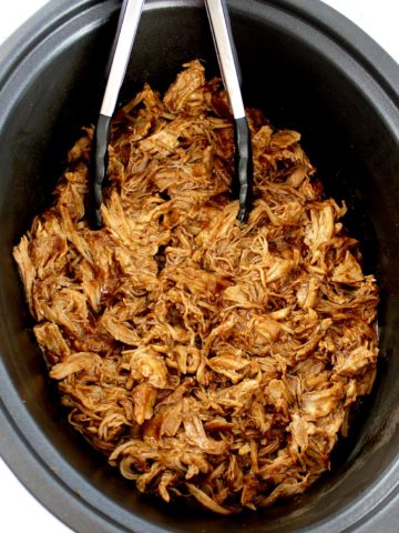 pulled pork in slow cooker insert with black tongs
