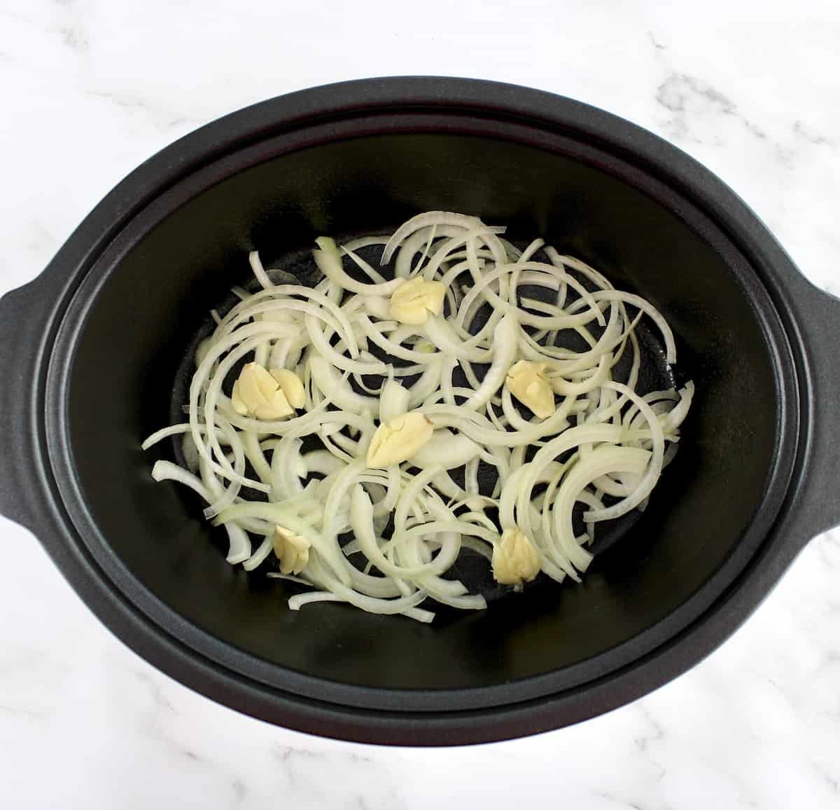 sliced onions and 6 smashed cloves of garlic in slow cooker insert