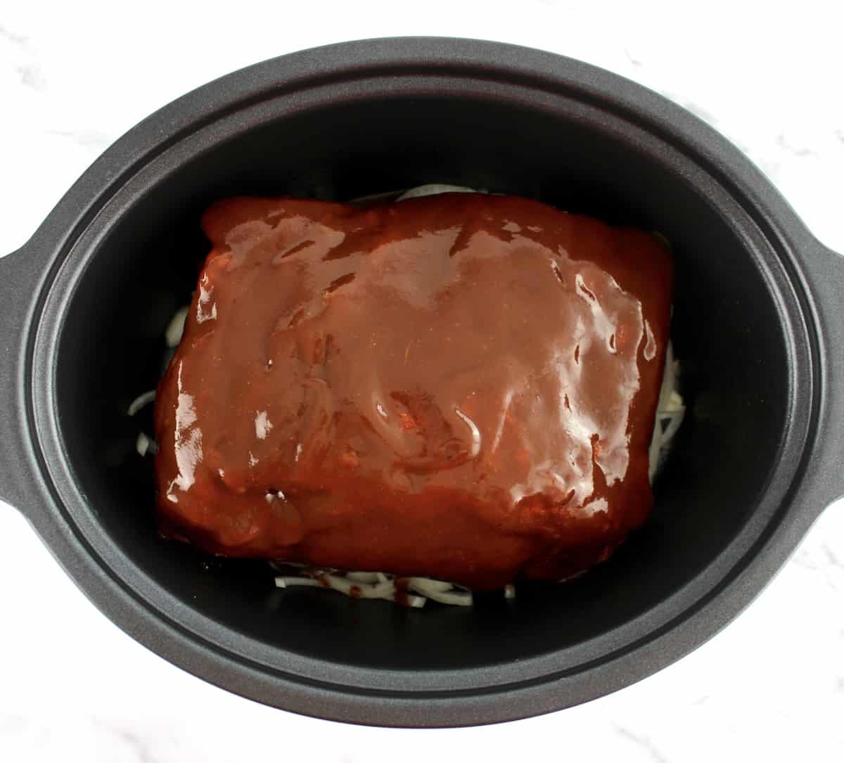 bbq sauce covered raw pork shoulder in slow cooker insert