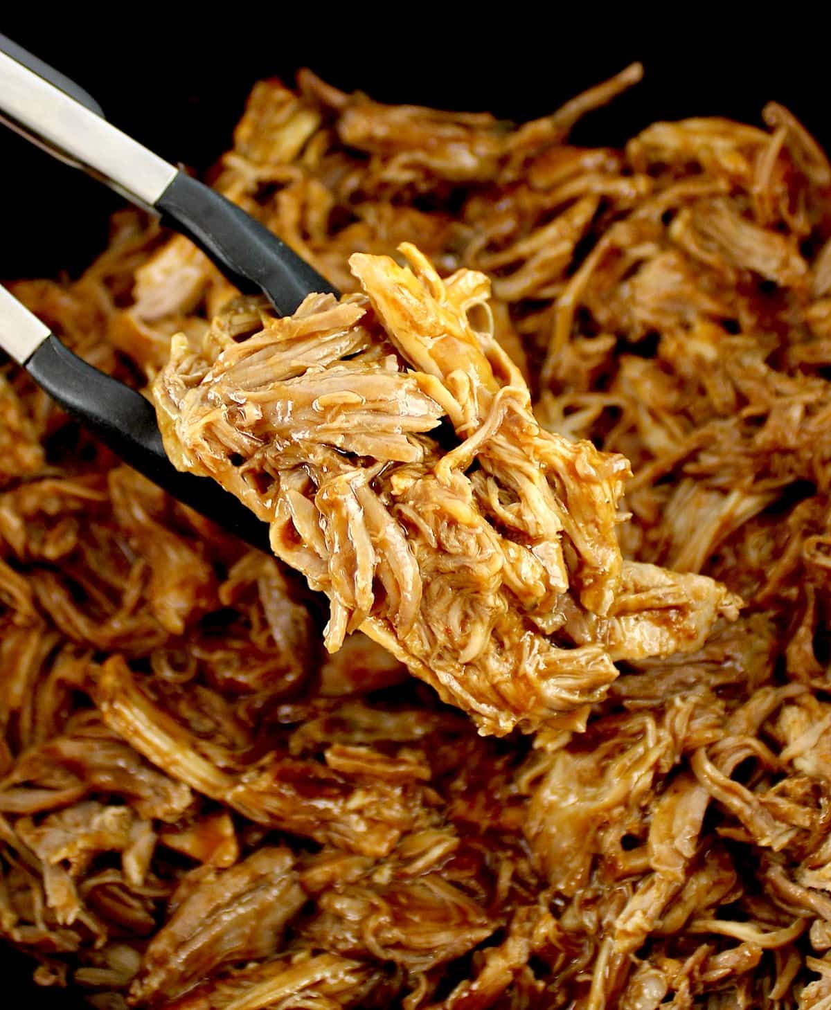 Slow Cooker Pulled Pork with tongs holding up some