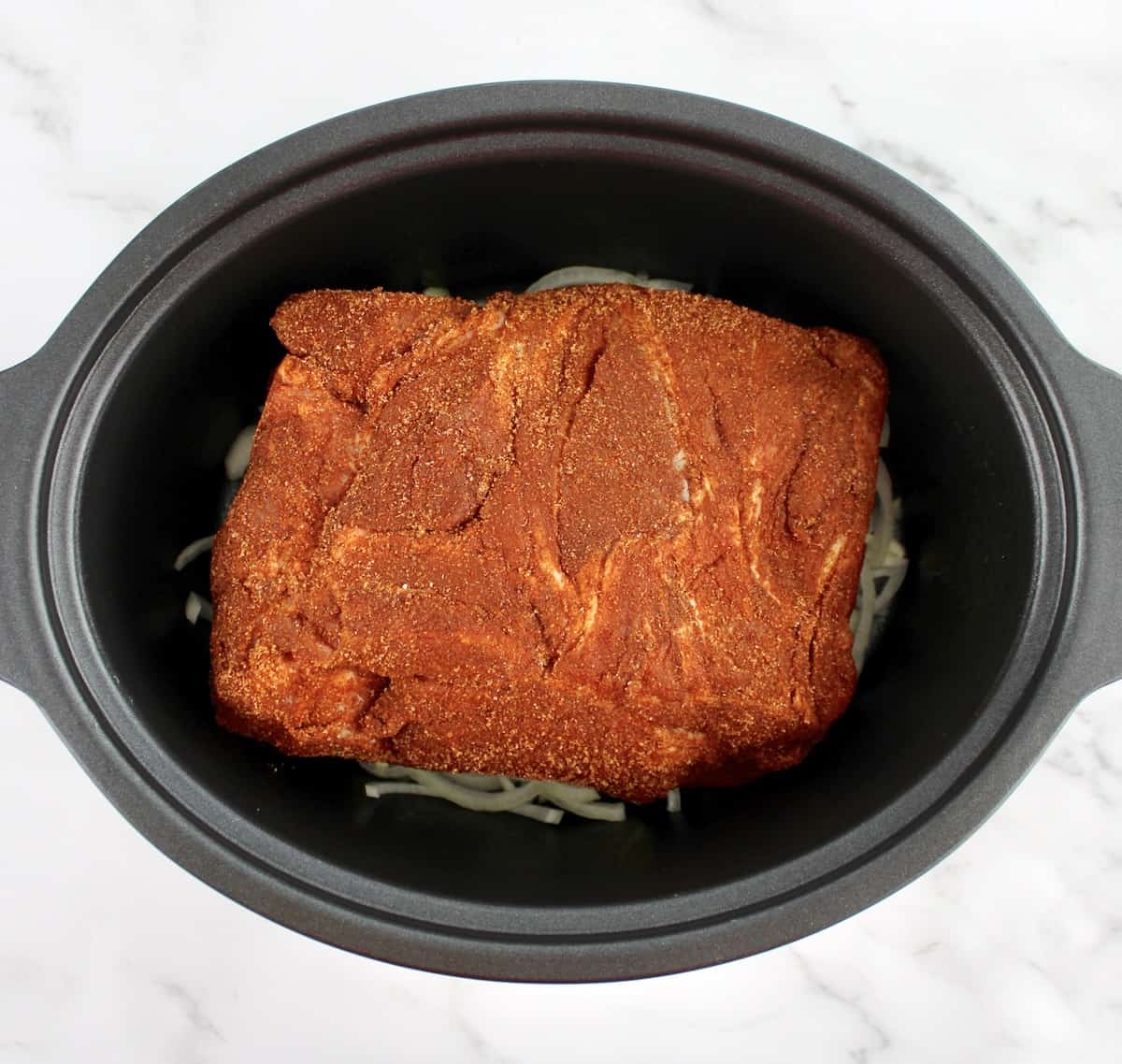 raw pork shoulder with bbq spice rub on it in slow cooker insert