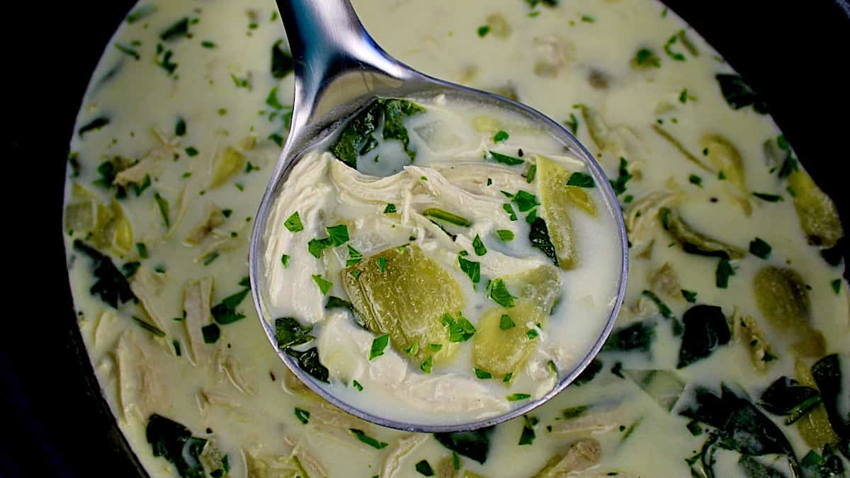 closeup of Slow Cooker Spinach Artichoke Chicken Soup in silver ladle with chopped parsley