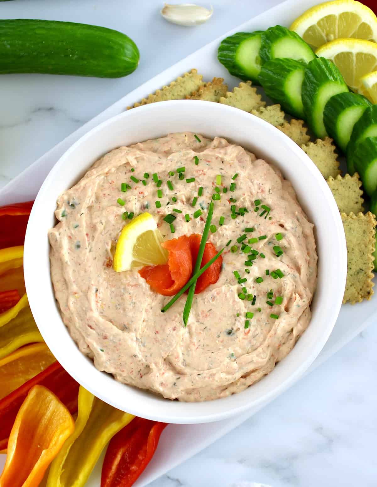 Smoked Salmon Dip in white bowl with mini peppers, crackers and cucumber slices on side