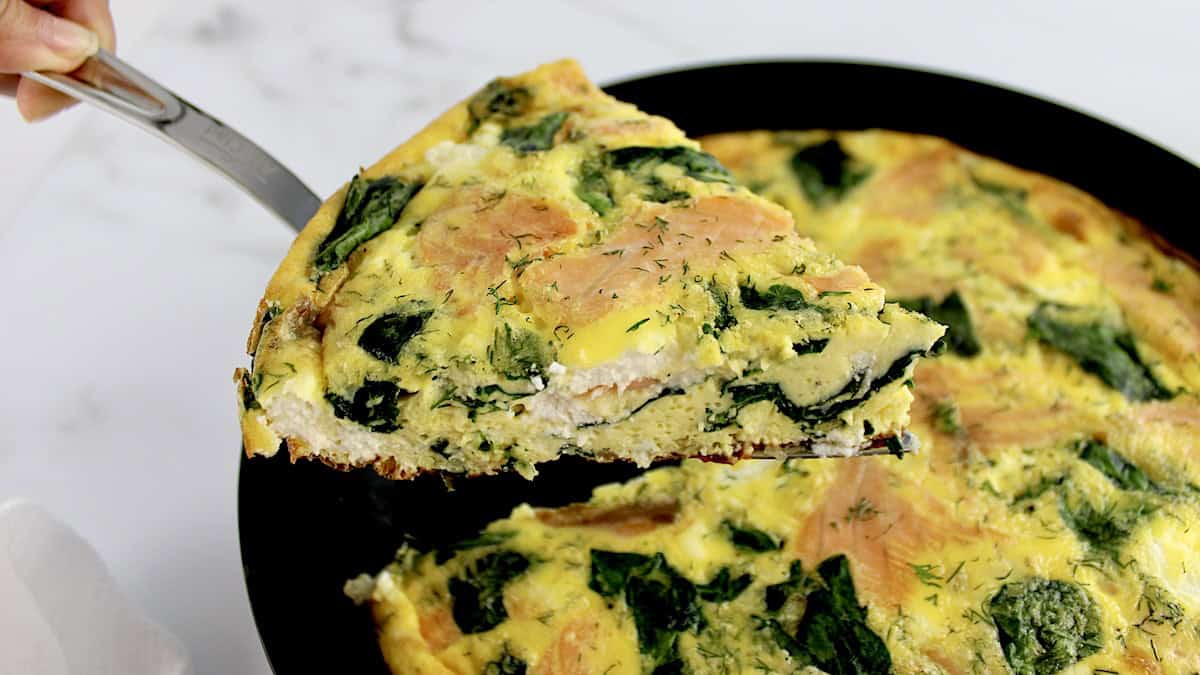 slice of Smoked Salmon and Spinach Frittata held up over cast iron skillet