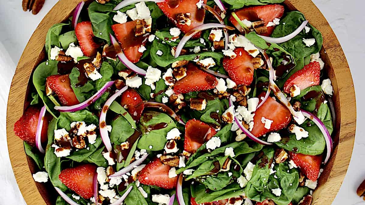 closeup of Strawberry Spinach Salad in wooden bowl with balsamic dressing