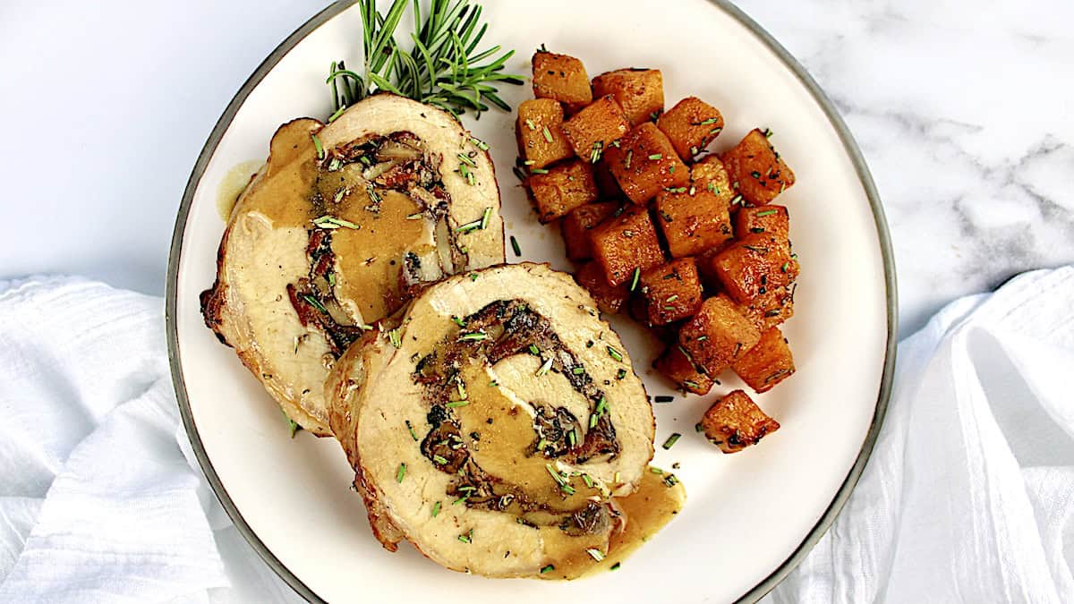 2 stuffed pork loin slices on white plate with cubes of butternut squash