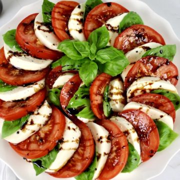 caprese salad arranged in a circle with fresh basil in the center and balsamic drizzled all over