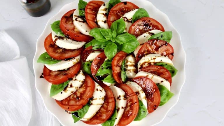 caprese salad arranged in a circle with fresh basil in the center and balsamic drizzled all over