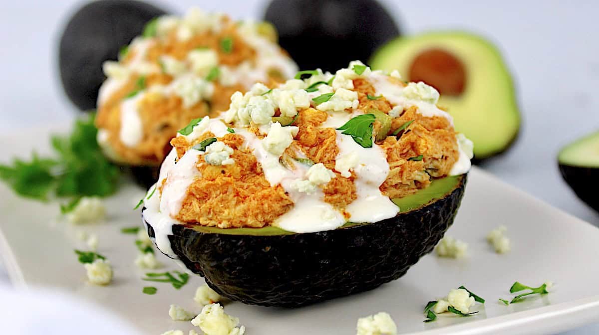Buffalo Chicken Stuffed Avocado with blue cheese drizzled on top and dripping off the side