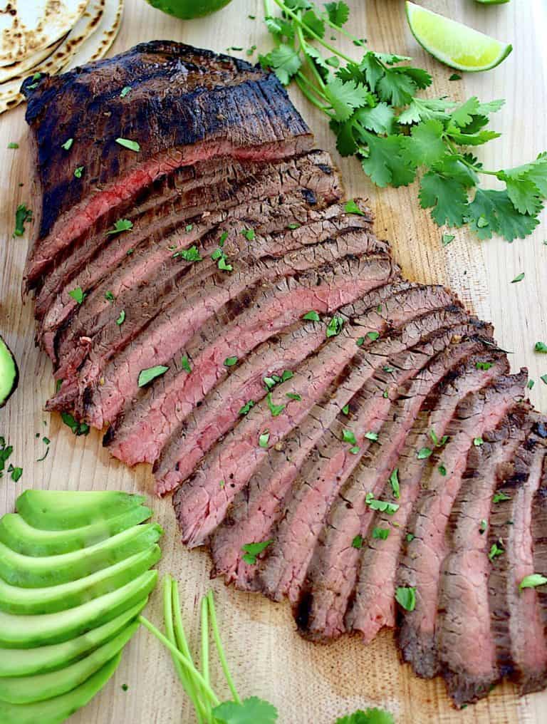 Carne Asada sliced on cutting board with sliced avocado with cilantro on side