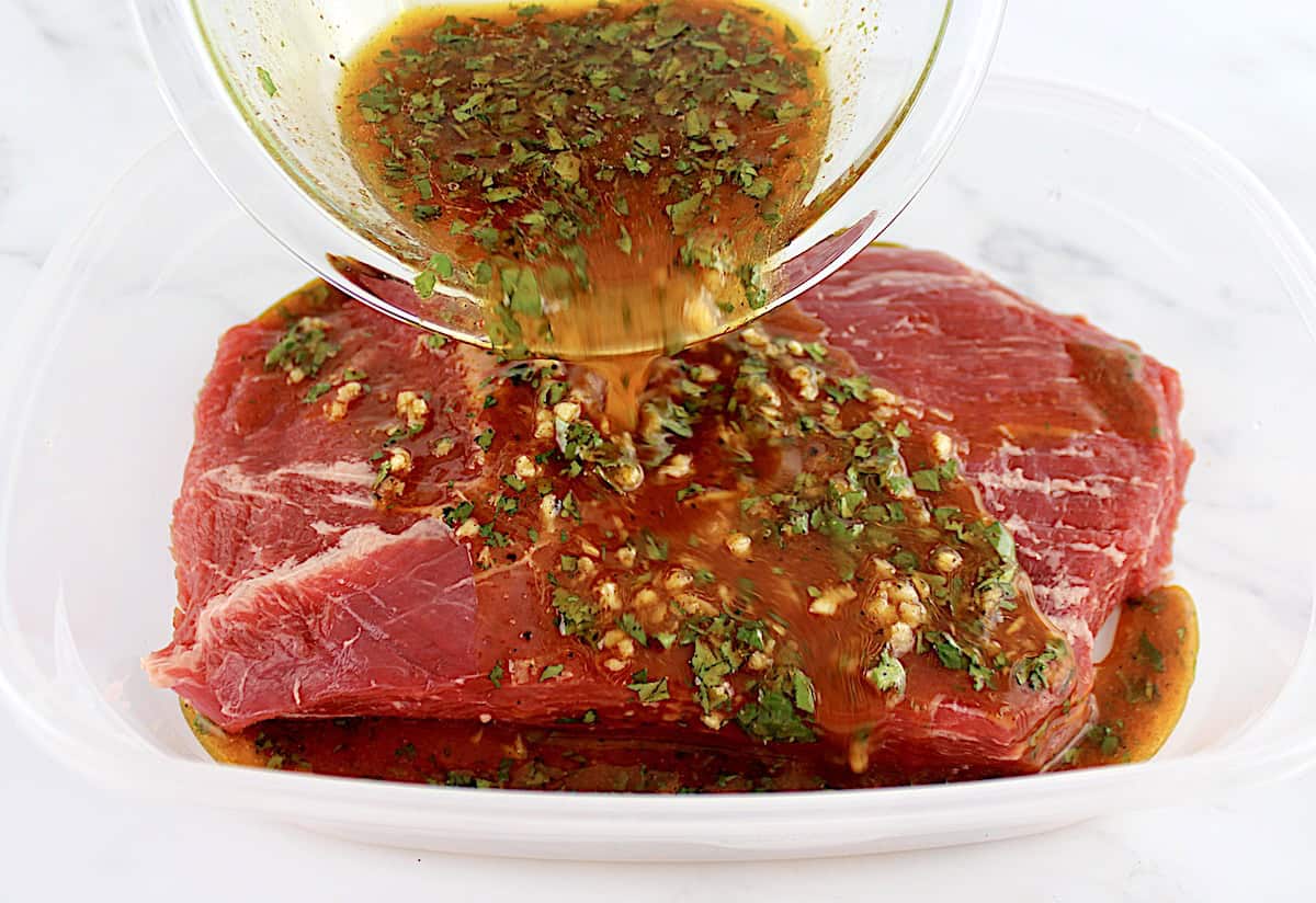 Carne Asada marinade being poured over flank steak in clear tupperware