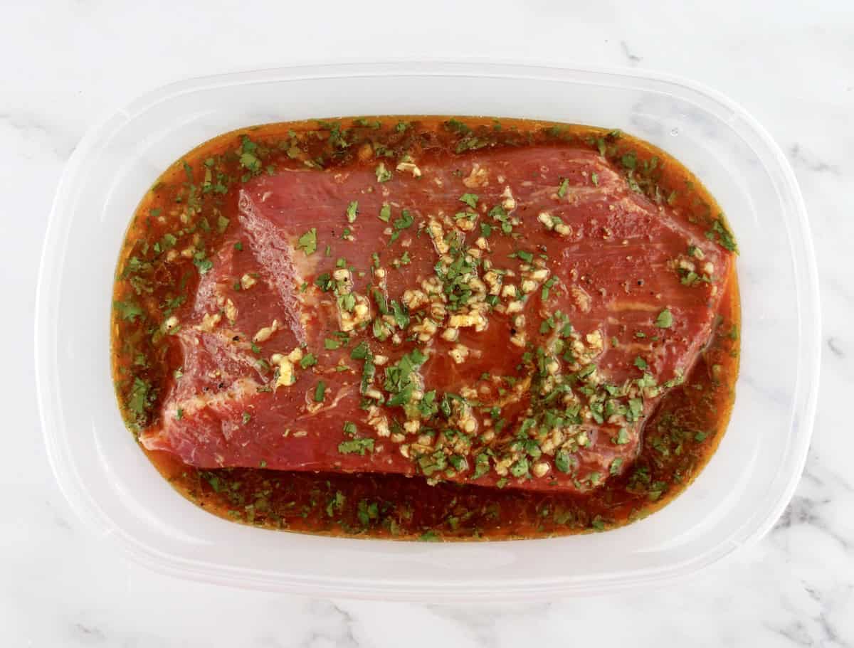 flank steak in clear open tupperware container with marinade