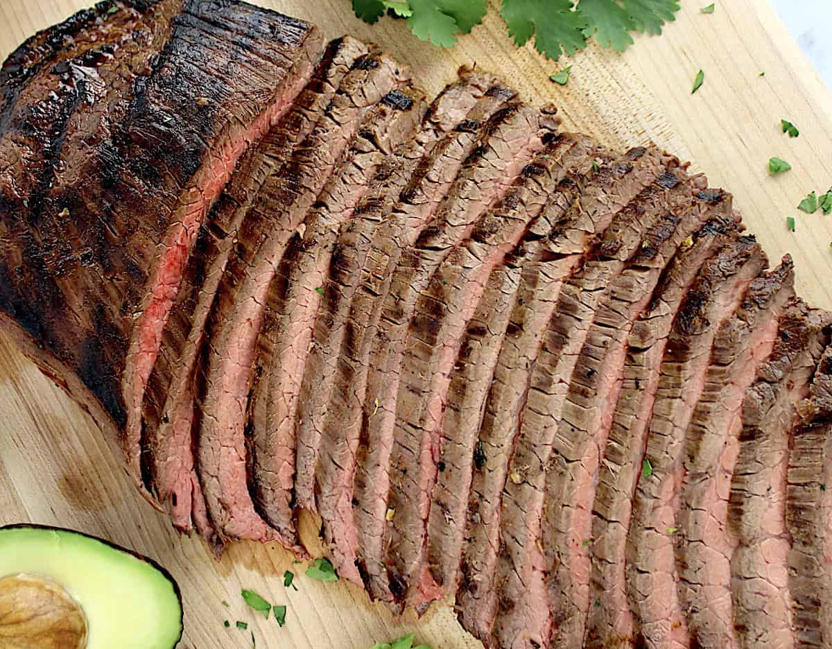 Carne Asada sliced up on cutting board with avocado and cilantro on side