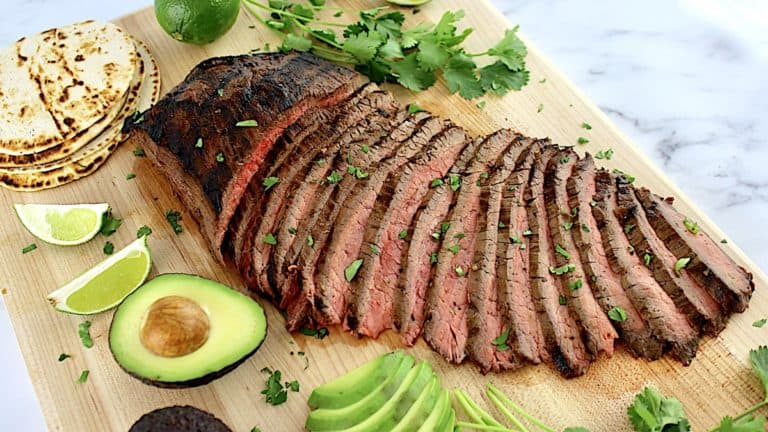 Carne Asada sliced on cutting board with sliced avocado with cilantro on side