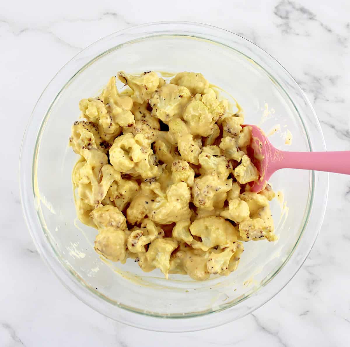 roasted cauliflower tossed with cheese sauce in glass bowl with pink spoon