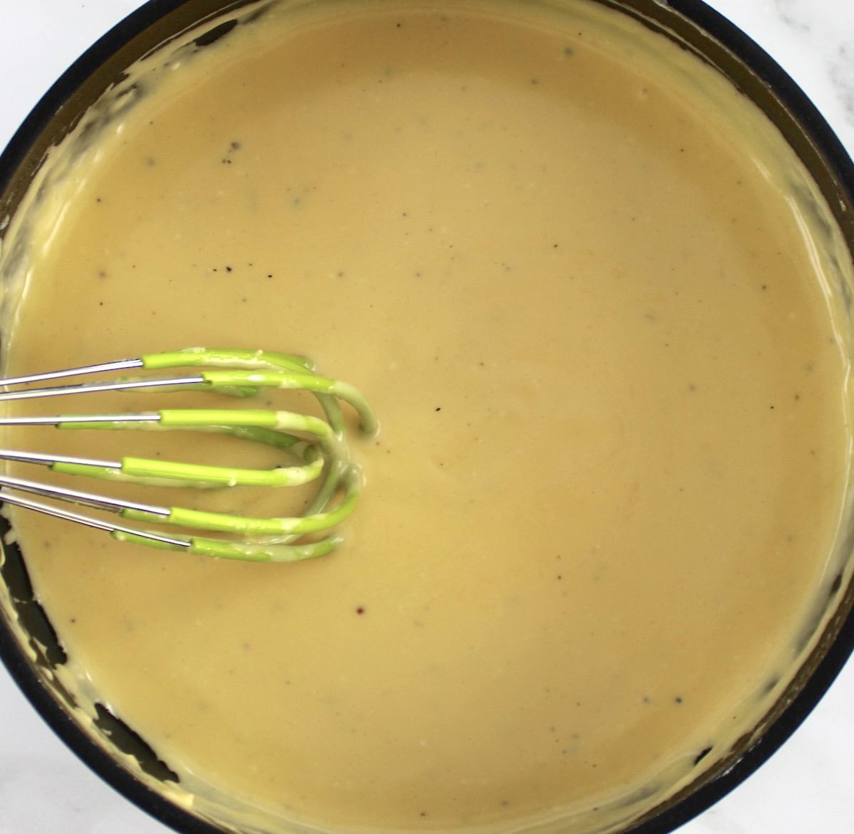 cheese sauce in saucepan with silicone whisk