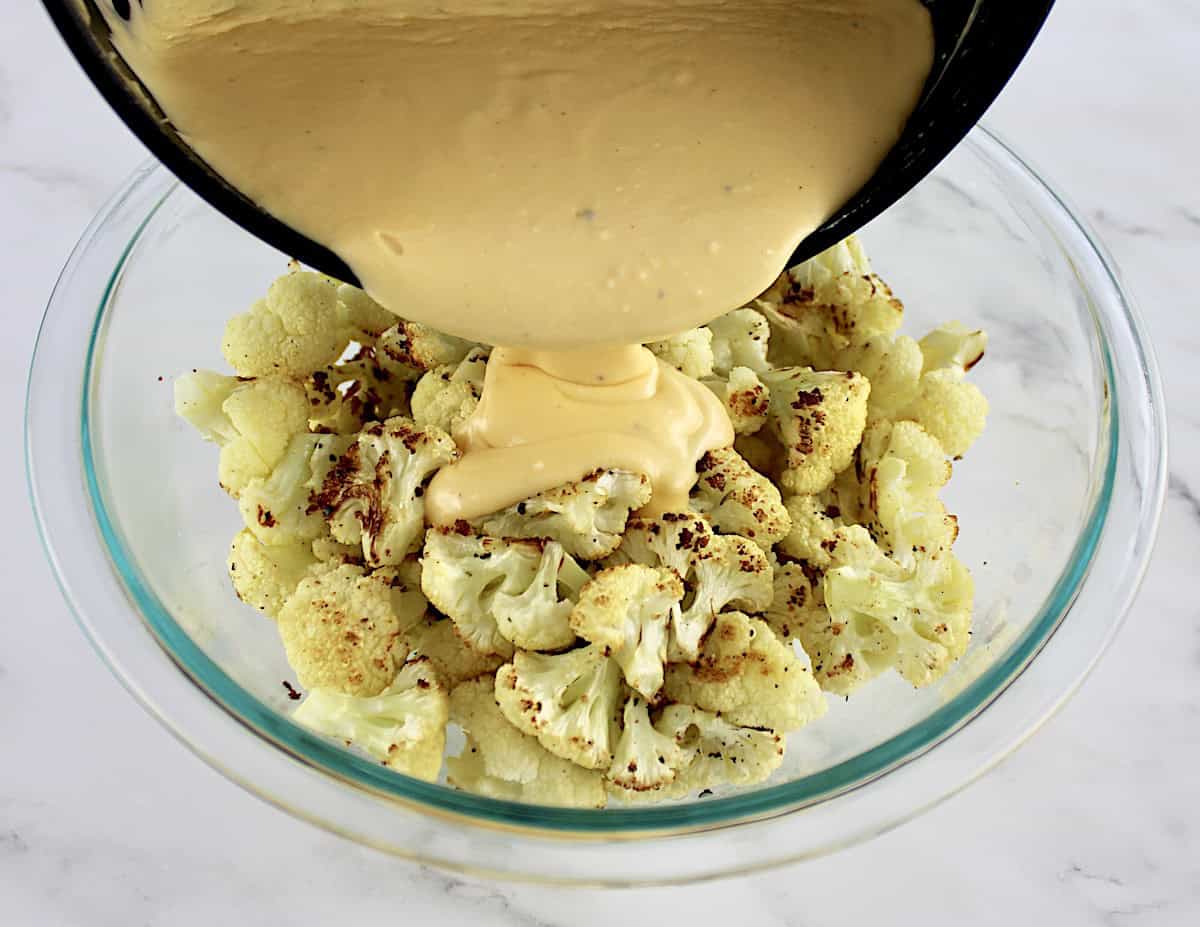 cheese sauce being poured from saucepan into glass bowl with roasted cauliflower