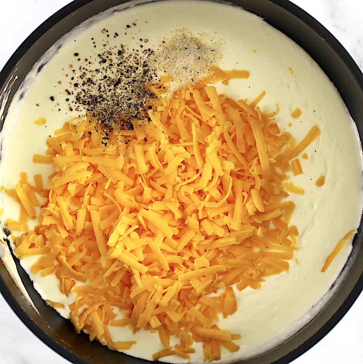 shredded cheddar cheese, pepper and garlic salt with cream in saucepan