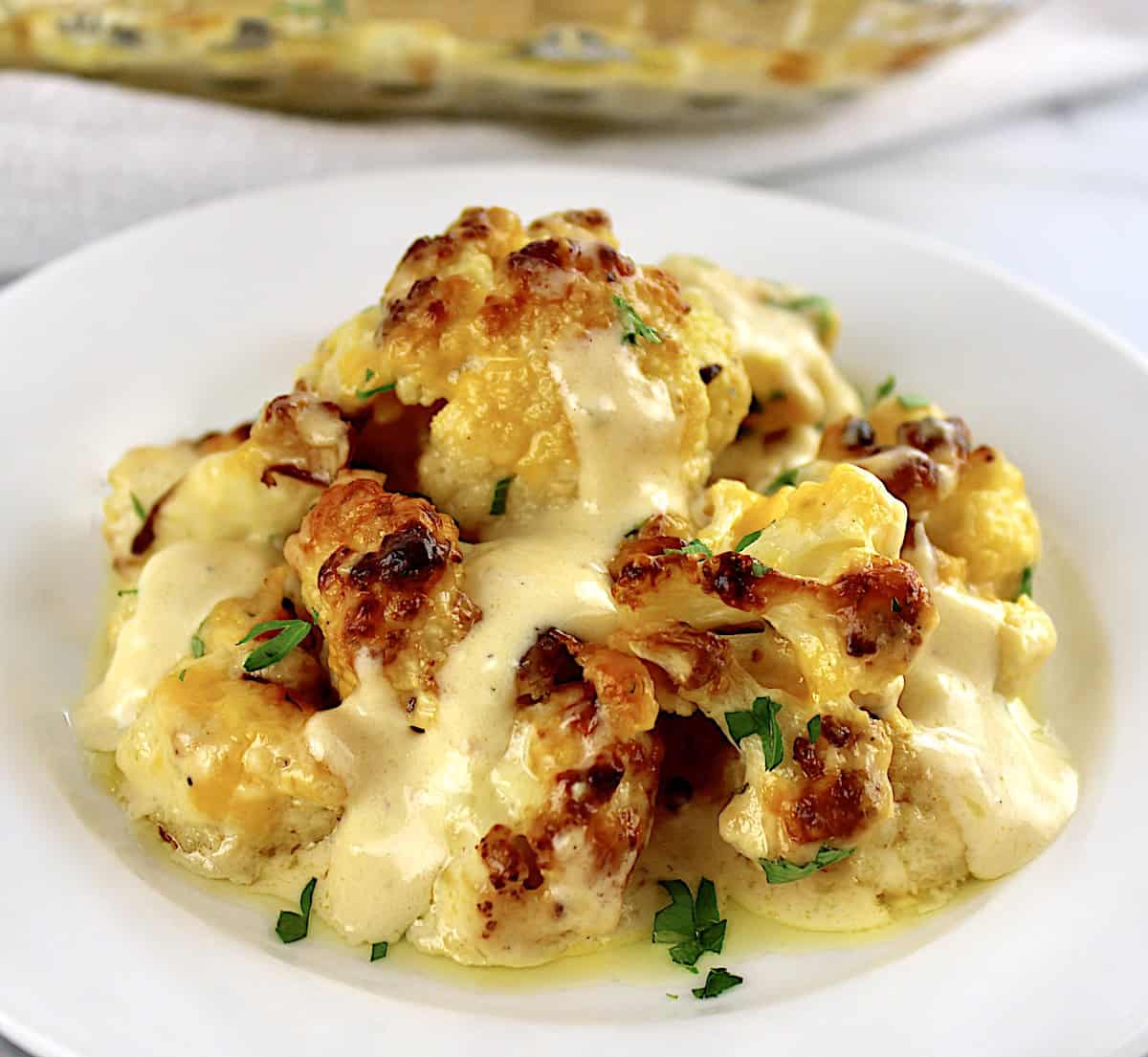 closeup of Cheddar Roasted Cauliflower on white plate with chopped parsley