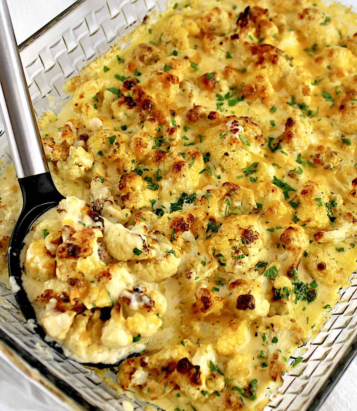 Cheddar Roasted Cauliflower in glass casserole with serving spoon on side