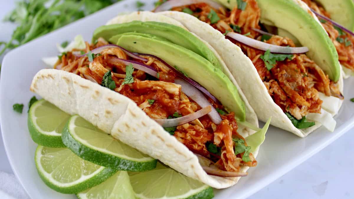 closeup of Chicken Tinga in tortillas on white plate with limes slices on side