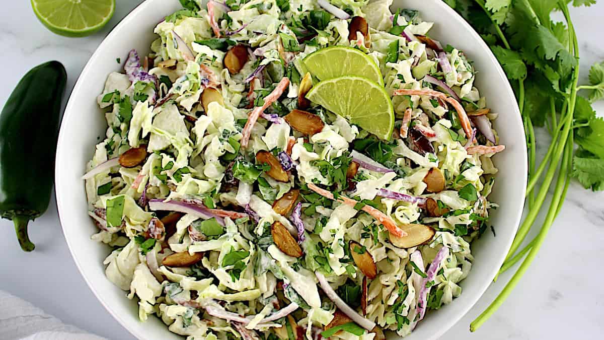 Cilantro Lime Coleslaw in white bowl with 2 lime slices on top