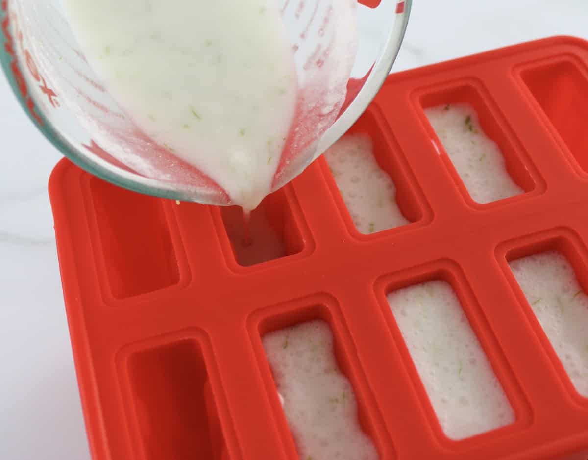 Coconut Lime Popsicles base mixture being poured into red popsicle molds
