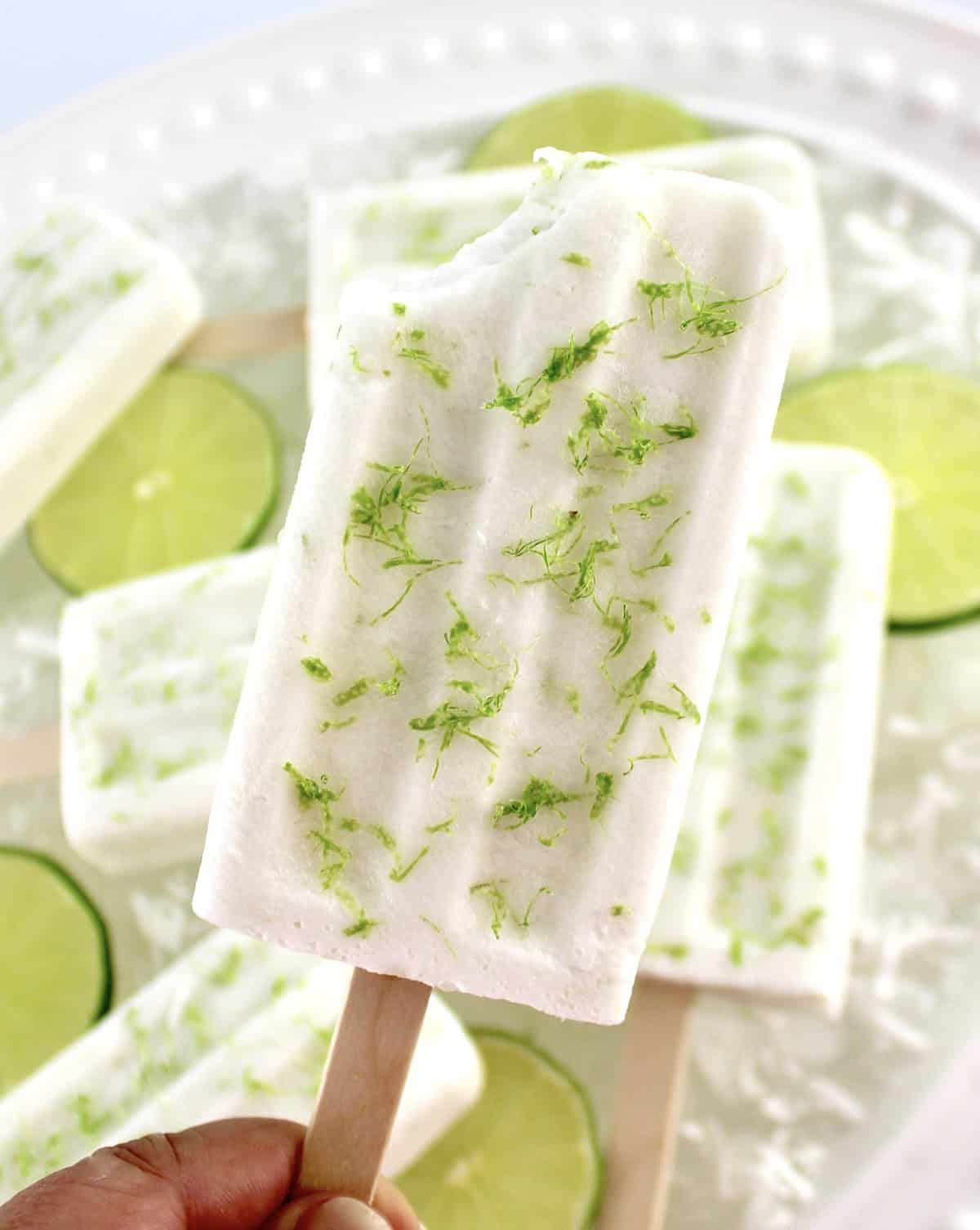 holding up Coconut Lime Popsicle with lime zest and bite missing with more popsicles in background