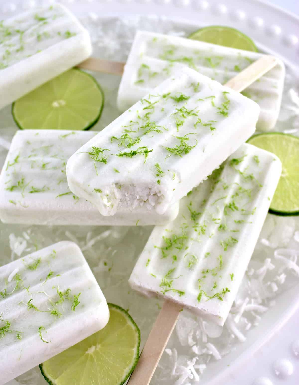 overhead view of 6 Coconut Lime Popsicles on ice with lime slices and bite taken out of one on top