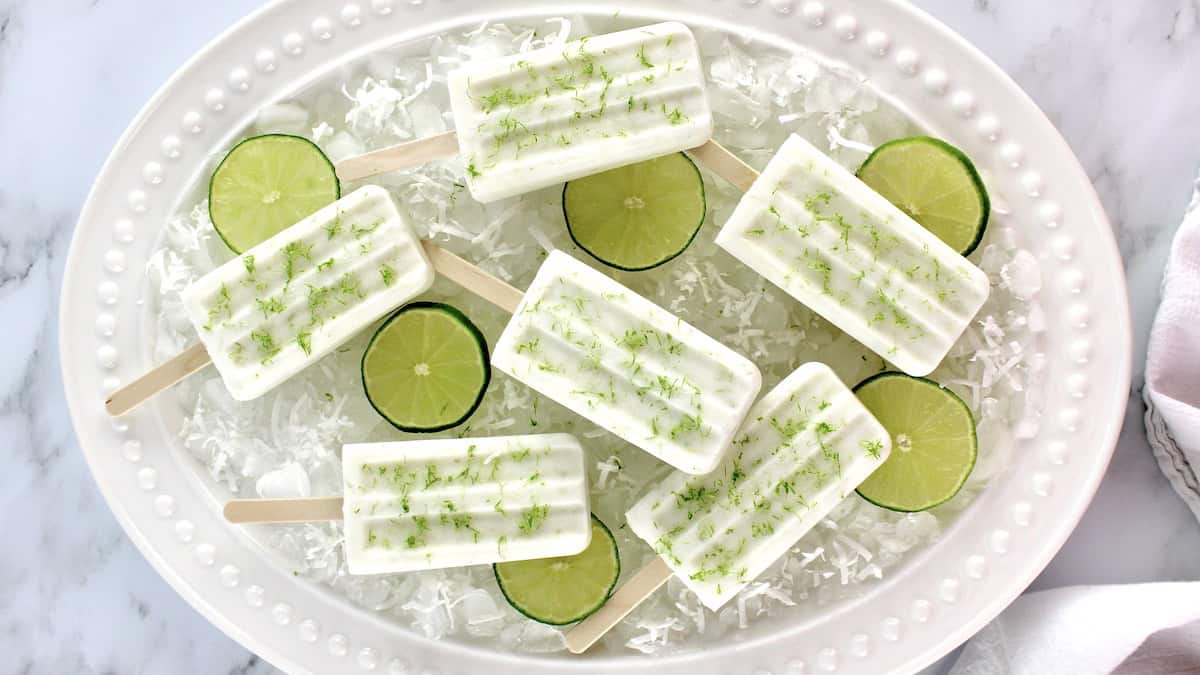 overhead view of 6 Coconut Lime Popsicles on ice in oval platter with lime slices