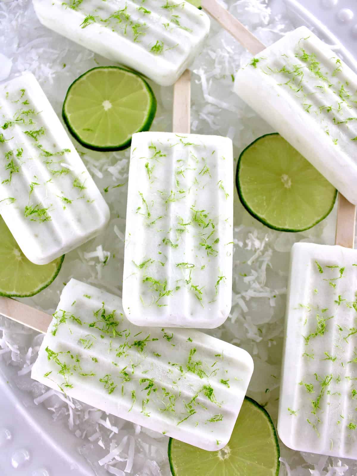 overhead view of 6 Coconut Lime Popsicles on ice with lime slices