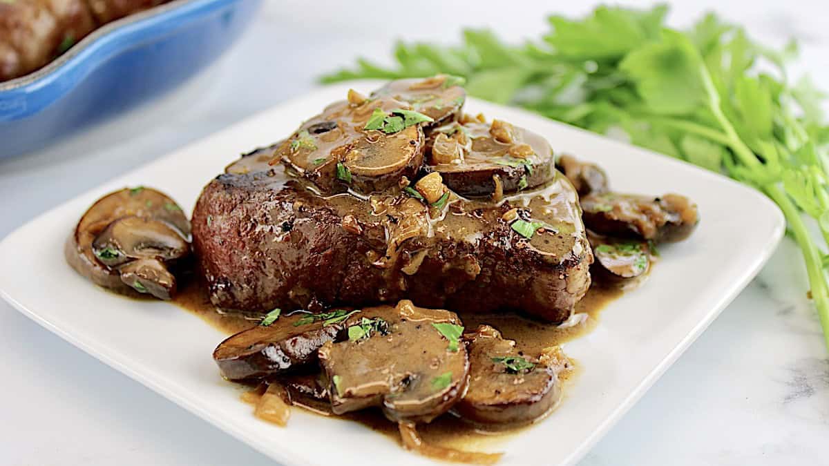 Filet Mignon with Mushroom Sauce on top on white plate with fresh parsley in background