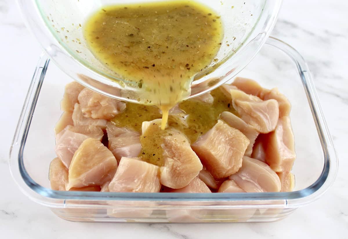 marinade being poured over chunks of raw chicken in glass container