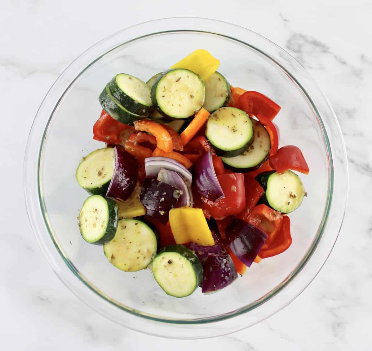sliced peppers, red onion and zucchini in glass bowl with marinade poured over