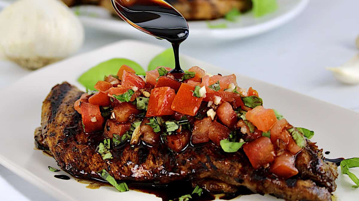 Grilled Chicken Bruschetta on white plate with balsamic being spooned over top