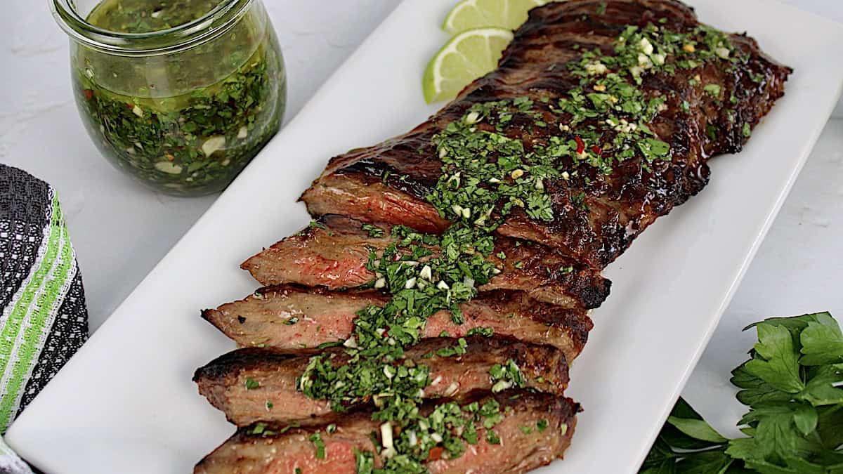 Grilled Skirt Steak Chimichurri sliced on white plate with chimichurri sauce