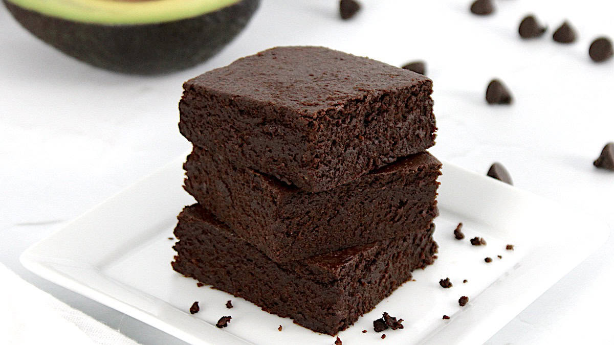 3 Keto Avocado Brownies stacked up with half a avocado in the background