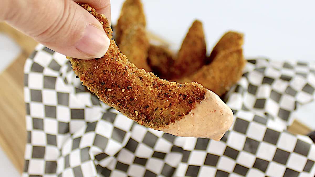 holding keto Avocado Fry with zesty dipping sauce on the end