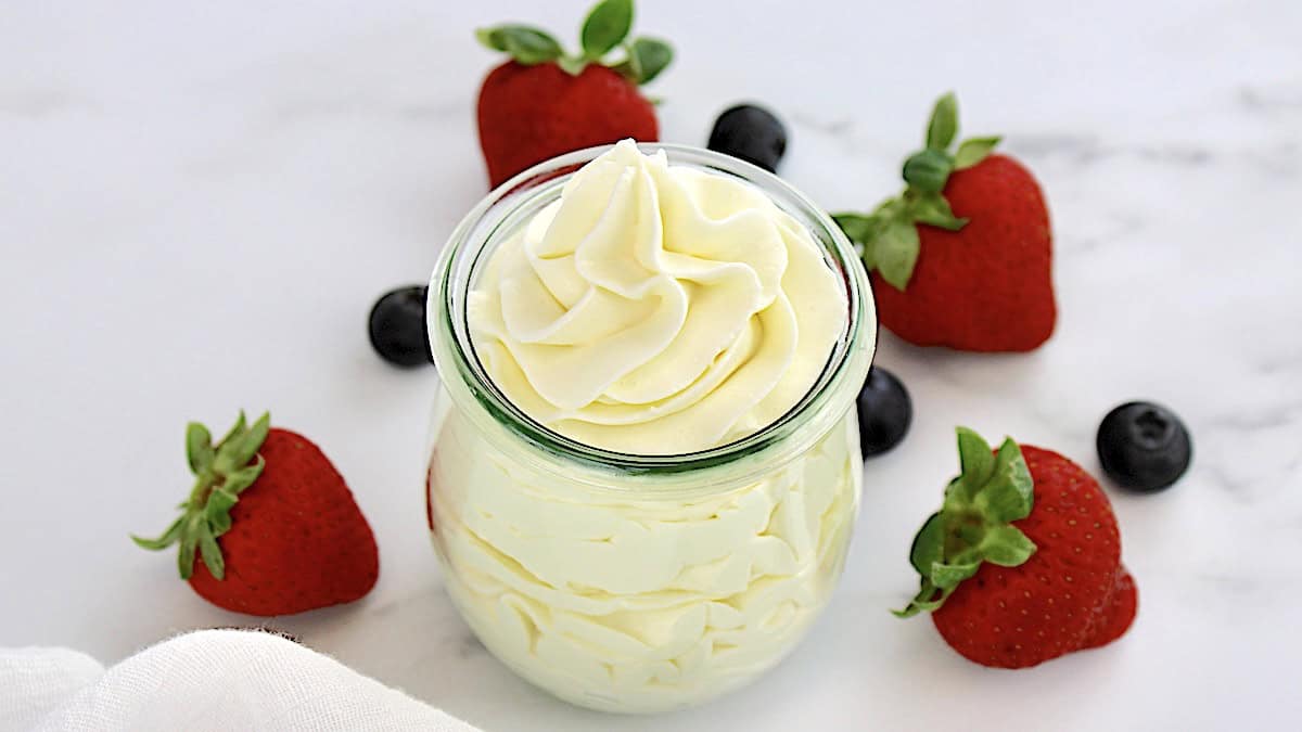 Keto Cheesecake Fluff in open glass jar with strawberries and blueberries in back