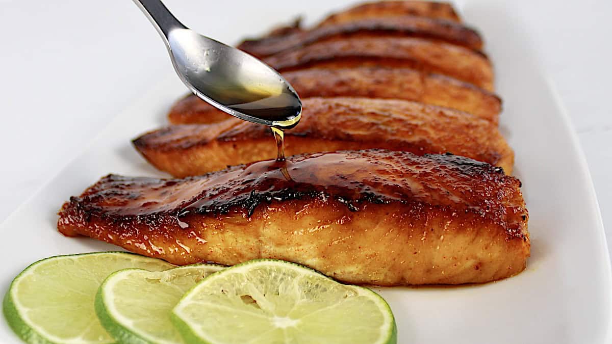 Keto Maple Glazed Salmon with syrup being spooned over top and lime slices on side