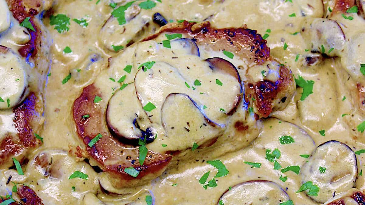 closeup of Keto Smothered Pork Chops in skillet with mushrooms and sauce on top