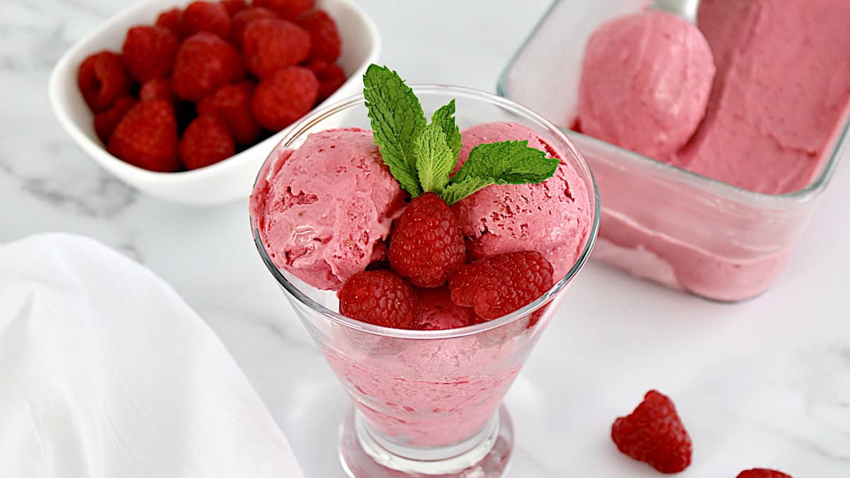 No Churn Raspberry Ice Cream in glass with mint sprig and 3 raspberries