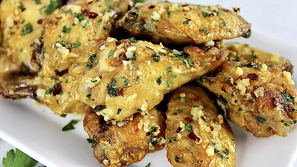 Parmesan Garlic Chicken Wings piled up on white plate with grated parmesan on top