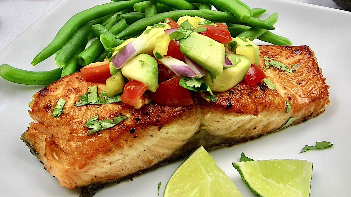 piece of salmon on white plate with salsa on top and green beans on the side